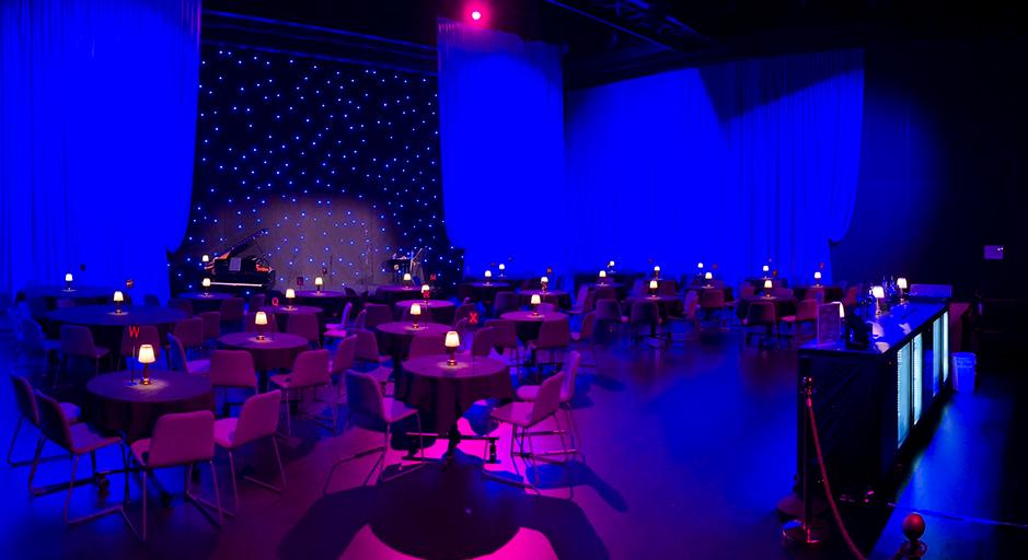 An empty room with tables and chairs, lit in blue light. 